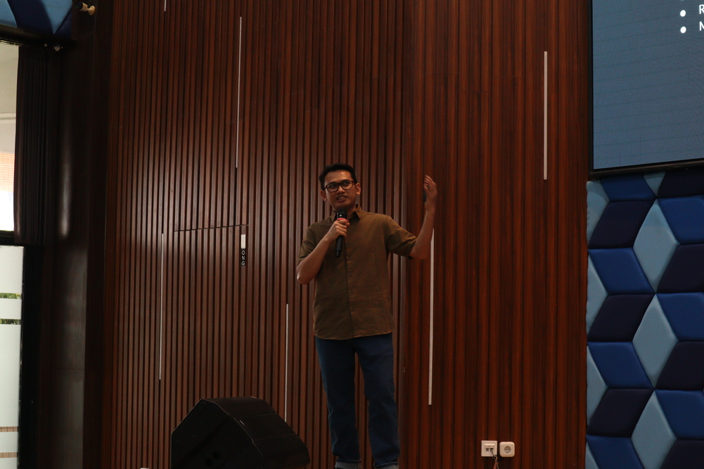 Pembicara mengangkat tangan saat menjelaskan materi kuliah tamu kepada mahasiswa